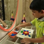 Kindergarten child making patterns with a mirror at Edistää Preschool, Wadala West, Mumbai